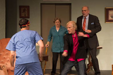 Mercutio, back to us, in blue nurses outfit and Aztec head band, Benvolio in thigh-length turquoise shirt and black pants and leaning on a cane, Tybalt in open sport jacket, bright chartreuse shirt and jeans, and Romeo in suit and tie with blue shirt. In the background, a gold easy chair, the elevator, and paintings on the wall.